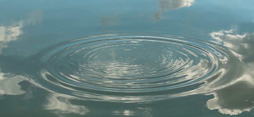header weerspiegeling en mindfulness. wateroppervlak wat een weerspiegeling geeft met waterringen in het midden